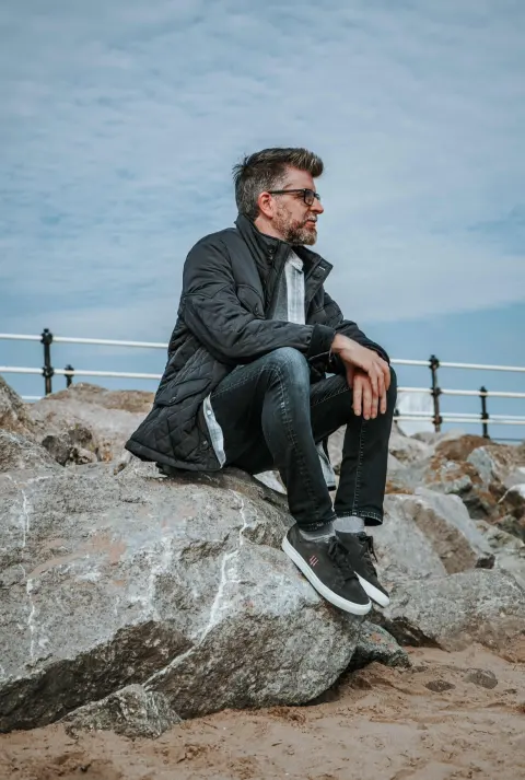 Phil Alderson seated on rocks by the sea