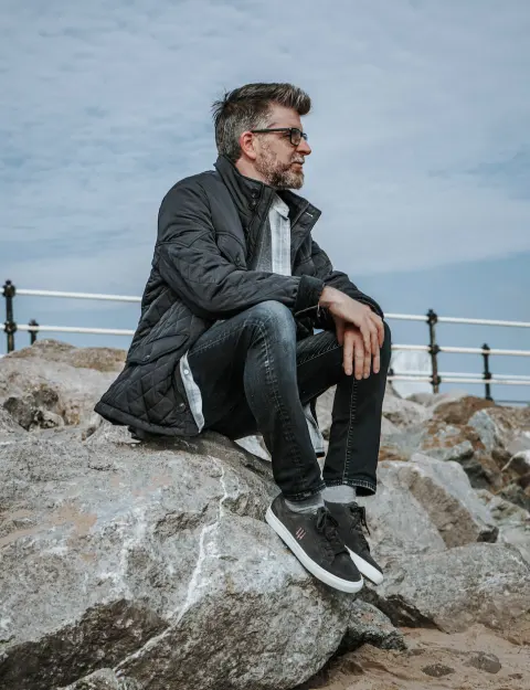 Phil Alderson seated on rocks by the coast